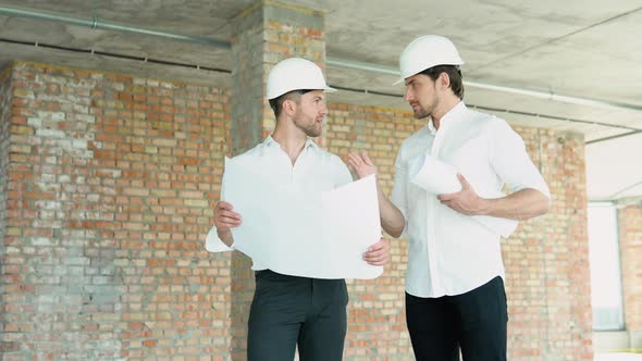A Young Engineers in Safety Helmets Standing on an Underconstruction Building Holding a Blueprint of