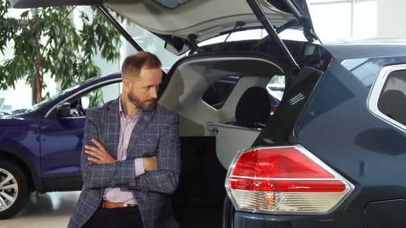 A Young Seller in a Suit Sits at the Open Trunk of the Car