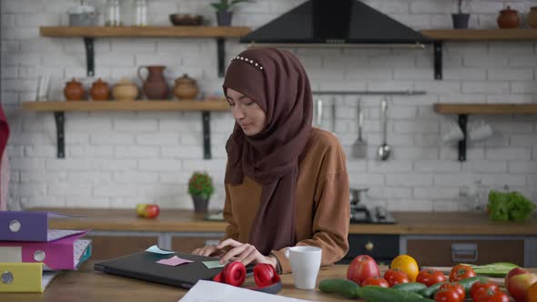 Confident Beautiful Woman in Hijab Drinking Morning Coffee Opening Laptop Putting on Headphones in