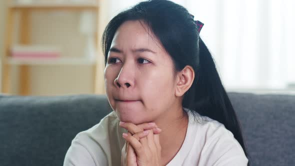Depressed crying Asian business woman stressed with headache sitting on sofa in living room.