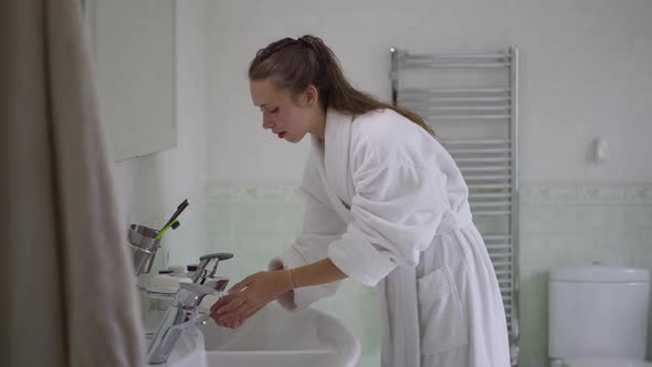 Slim Charming Caucasian Woman in White Bathrobe Turning on Faucet and Washing Face in Slow Motion