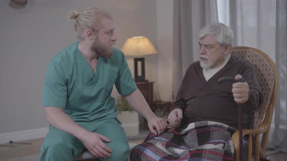 Portrait of Caucasian Man Listening To Stories of Upset Retiree in Nursing Home and Holding His Hand