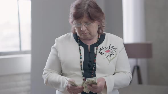 Sad Redhead Senior Woman in Eyeglasses Counting Money Throwing Away Dollars and Leaving