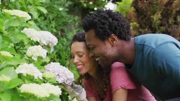 Happy biracial couple gardening together, smelling flowers and laughing