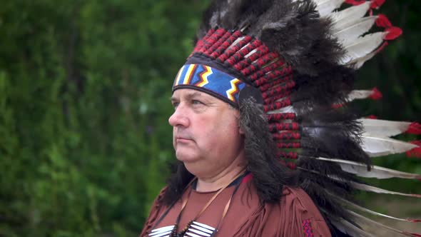 Old Native American Indians Greets Raising His Hand. Stands Against the Background of the Forest