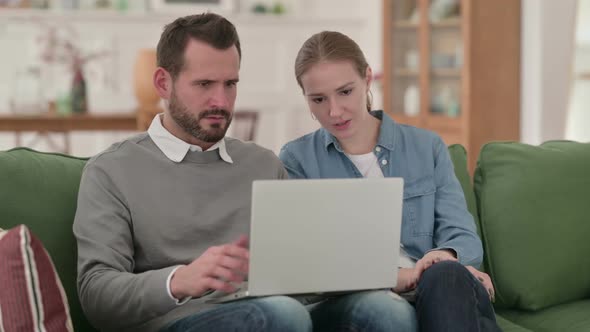 Couple Reacting to Loss on Laptop While Sitting on Sofa