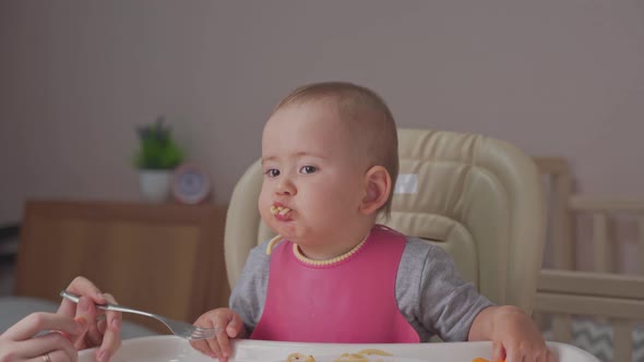 Toddler eats spaghetti sitting on a feeding chair.