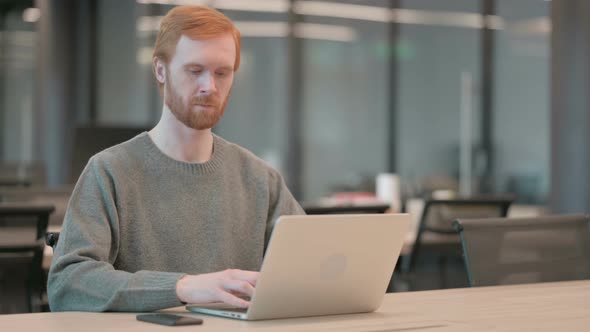 Young Man Smiling at Camera While Using Laptop in Office