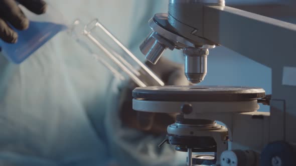 A Researcher in a Laboratory in Protective Rubber Gloves Pours a Blue Liquid Into a Test Tube