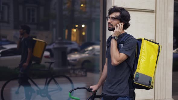 Delivery Man with Yellow Backpack Talk to a Client on the Street Using Earphones Slowmo