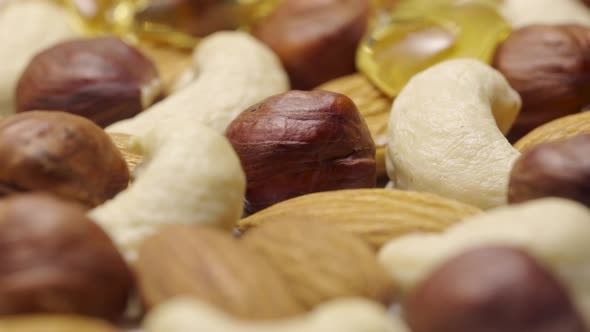 Stream of Golden Honey Flows and Envelops Mix of Almonds Cashews and Hazelnuts in Slow Motion