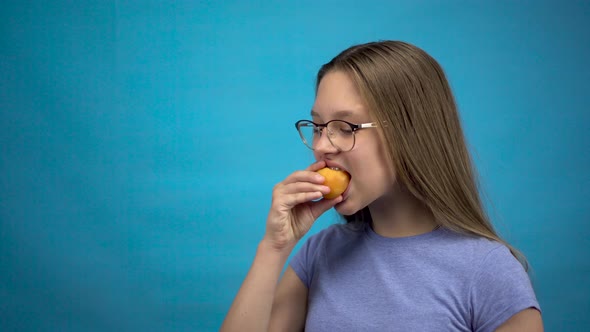 Teenager Girl with Braces on Her Teeth Eats an Apricot on a Blue Background. Girl with Colored