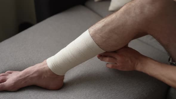 Man is Bandaging His Leg with an Elastic Bandage