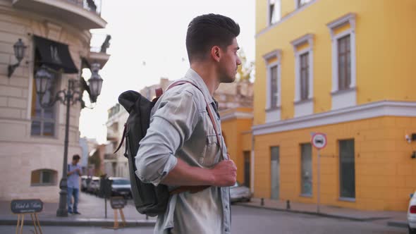 Attractive Young Handsome Man Tourist with Backpack Walking in City Center and Looking Around Slow