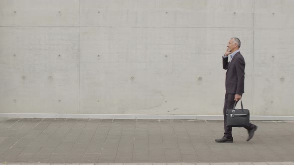 Businessman walking in front of concrete wall talking on the phone