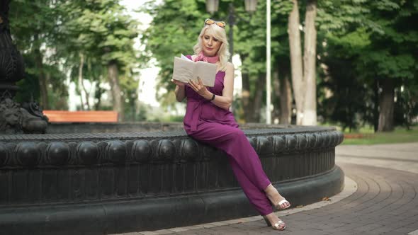 Wide Shot Elegant Slim Intelligent Woman Reading Book Sitting on Fountain in Urban Park on Summer