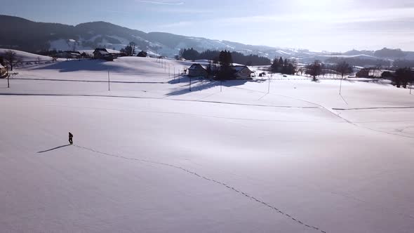 Young man walks through a big snowy field in the winter in Switzerland.