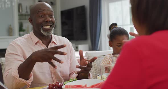 Happy african american grandfather talking, eating lunch with family at home