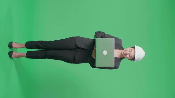 Full Body Of Asian Female Engineer With Safety Helmet Using A Laptop In The Green Screen Studio