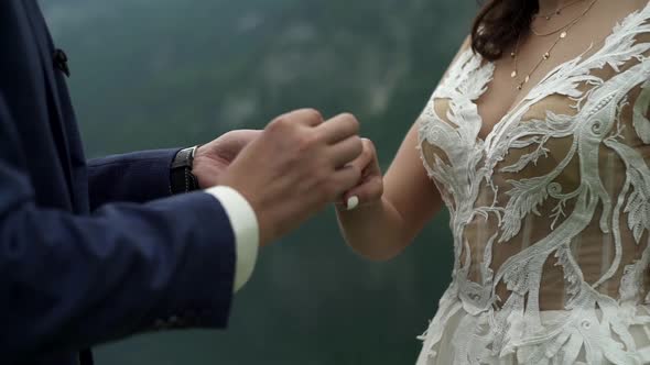 Groom puts bridal ring on bride's finger. Wedding ceremony on lake in mountains, traditional symbols