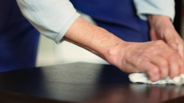 Active pensioner carries out dust cleaning. An elderly man wipes the dust off the table with a rag.