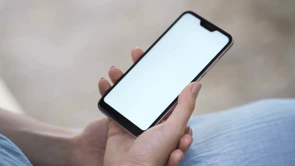 Female Hand Holding Smartphone with White Screen. Girl Using Mobile Phone While Walking in the