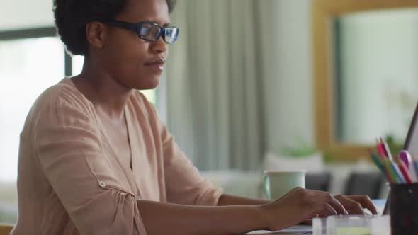 Happy african american woman sitting at table using laptop