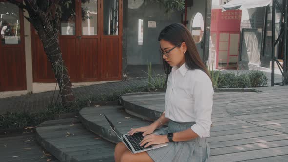 Asian Attractive Young Woman Wearing Glasses Working at Her Laptop on the Street