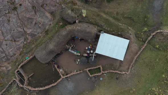 Aerial drone bird's eye view over a small cottage boundered by stone walls beside inca terrace farms