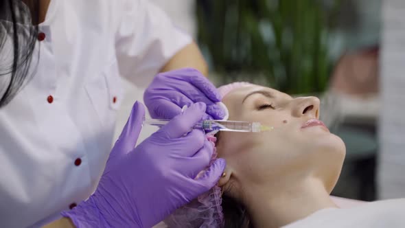 An experienced cosmetologist conducts mesotherapy for a woman who lays on a couch
