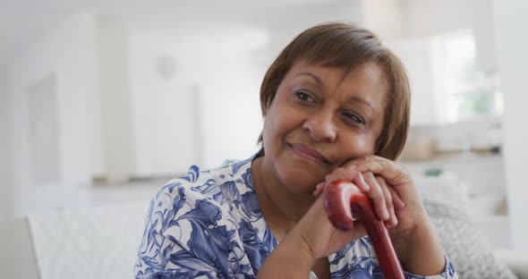 Happy african american senior woman sitting leaning on walking stick, looking away smiling