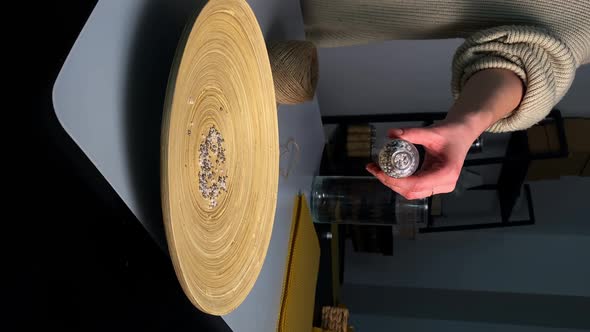 Woman Pours Small Beads From Glass Bottle Onto Ceramic Plate