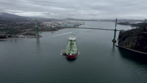 Barge and pilot boat passing under First Narrows or Lions Gate Bridge with landscape in background.