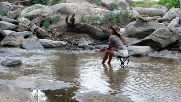 Rear view of a young Asian woman sitting and relaxing on a chair in waterfall stream