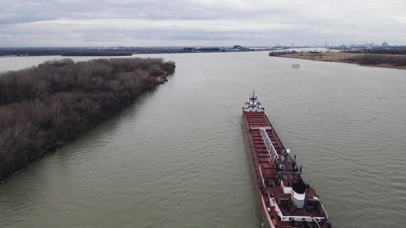 Tanker ship transporting material towards Detroit on vast river. Shipping near small island. Aerial