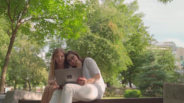 Young Woman Helping Her Old Retired Mother on a Laptop Sitting in a Park. Concept of Age Inclusivity