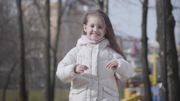 Portrait of Joyful Little Girl Grimacing at Camera in Autumn or Spring Park. Happy Smiling Caucasian