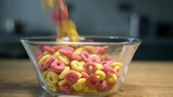 Pouring colorful breakfast cereal rings into glass bowl. Close up