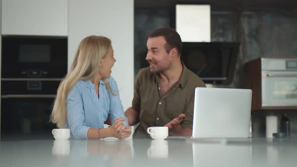 Happy Excited Couple Cheering Satisfied with Results on Laptop Drinking Coffee in Kitchen