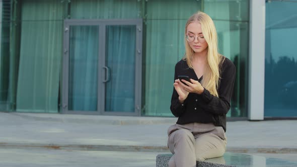 Blonde Young Caucasian Female Student Sitting Outdoor Holding Mobile Phone Surfing Internet Received