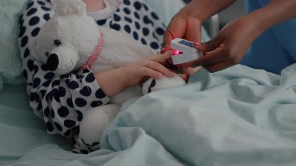 Closeup of Black Nurse Putting Medical Oximeter on Sick Child Finger Analyzing Heartbeat Pulse