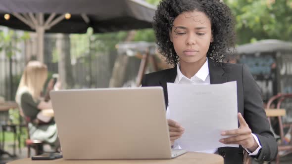 African Businesswoman Reading Documents While Sitting in Outdoor Cafe