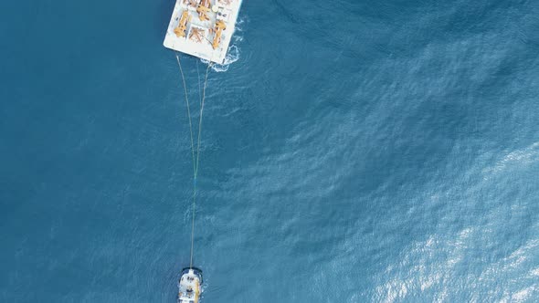 Construction equipment  on a floating barge being towed through the ocean by a tugboat. Drone view l