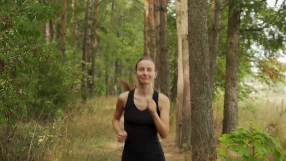 Young Woman is Jogging Along a Forest Road Against the Background of a Pine Forest