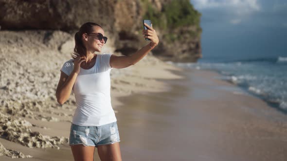 Beautiful Young Woman Takes a Selfie on a Smartphone at the Sandy Beach