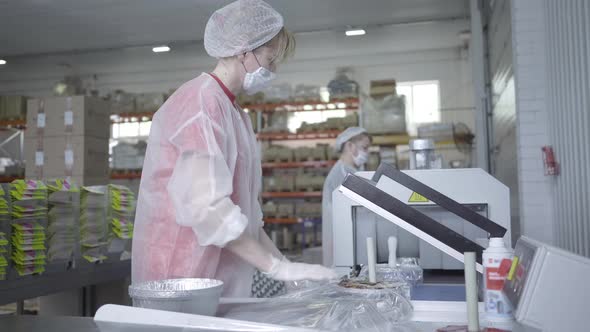 Side View of Confident Caucasian Woman in Face Mask and Uniform Packing Food Packaging Using