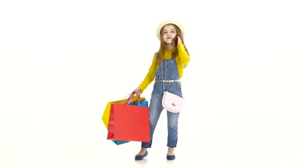 Little Girl Holding Bags and Talking on the Phone, Smiling. White Background