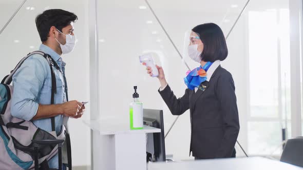 Caucasian female airline staff measuring body temperature of passenger before entering to airport.