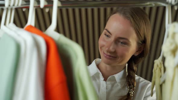 Young Woman Standing in Front of Hanger Rack and Trying to Choose Outfit