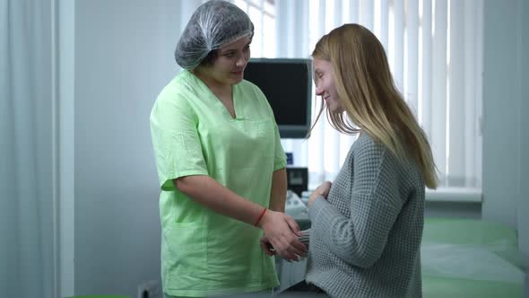 Positive Gynecologist Touching Pregnant Belly of Patient Sitting on Examination Couch Talking